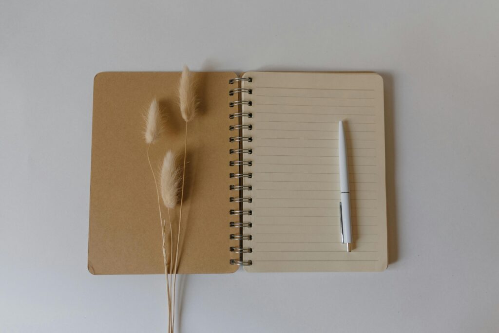 Open notebook with a pen and dried flowers on a simple beige backdrop. Perfect for work and organization themes.